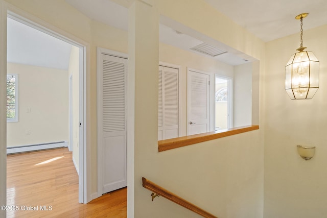 hall with a baseboard heating unit, light wood-type flooring, and an upstairs landing