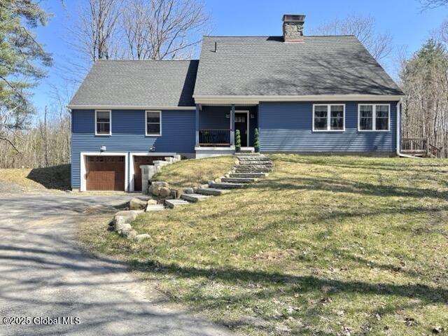 view of front facade with a chimney, an attached garage, driveway, and a front yard