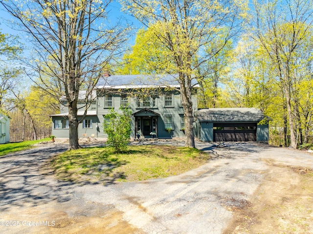 colonial home with dirt driveway, a chimney, and a shed
