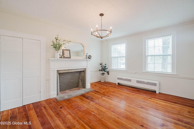 unfurnished living room with radiator heating unit, a chandelier, a fireplace, and wood-type flooring