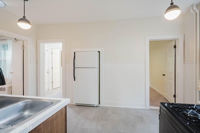 kitchen featuring freestanding refrigerator, gas stove, hanging light fixtures, light countertops, and a sink