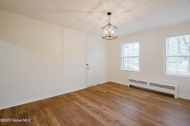 unfurnished dining area featuring radiator heating unit, wood finished floors, a chandelier, and baseboards