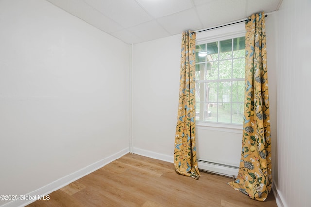 unfurnished room featuring a baseboard radiator, light wood finished floors, baseboards, plenty of natural light, and a drop ceiling