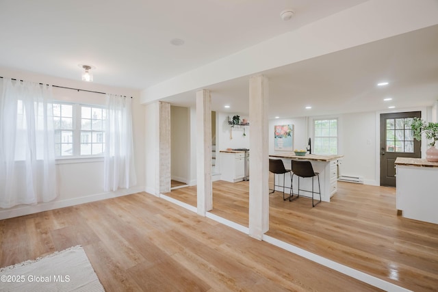 unfurnished living room with a baseboard radiator, light wood-style flooring, baseboards, and recessed lighting
