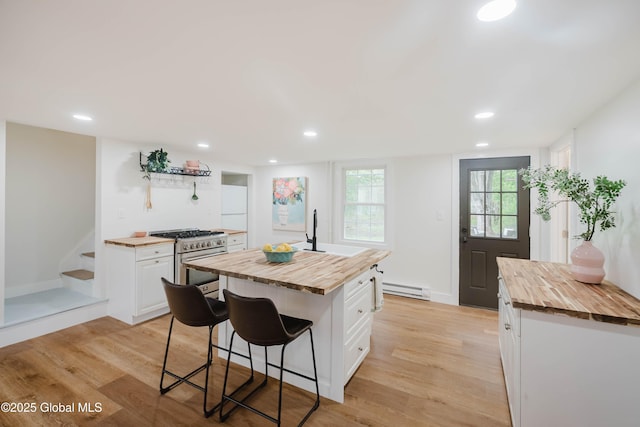 kitchen featuring wooden counters, high end stainless steel range oven, baseboard heating, white cabinetry, and a breakfast bar