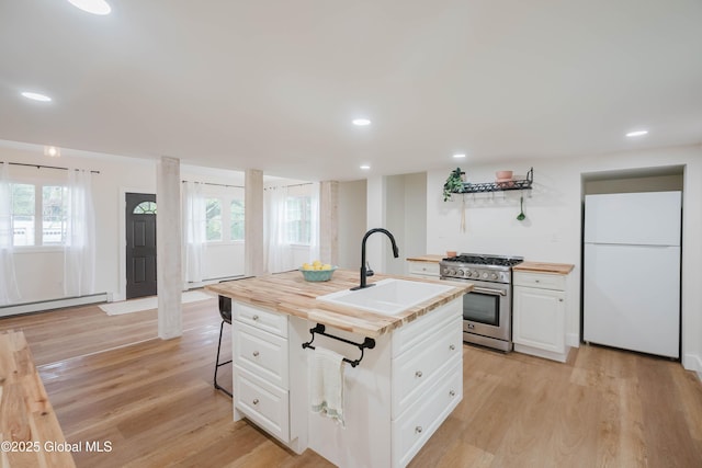 kitchen with freestanding refrigerator, high end stainless steel range oven, a sink, a baseboard heating unit, and wooden counters