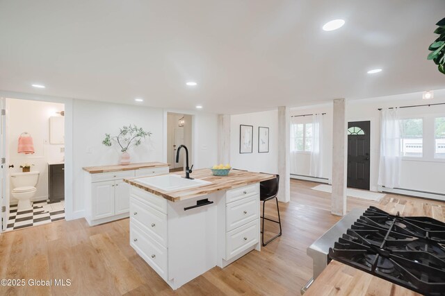 kitchen with wooden counters, a sink, a baseboard radiator, baseboard heating, and healthy amount of natural light