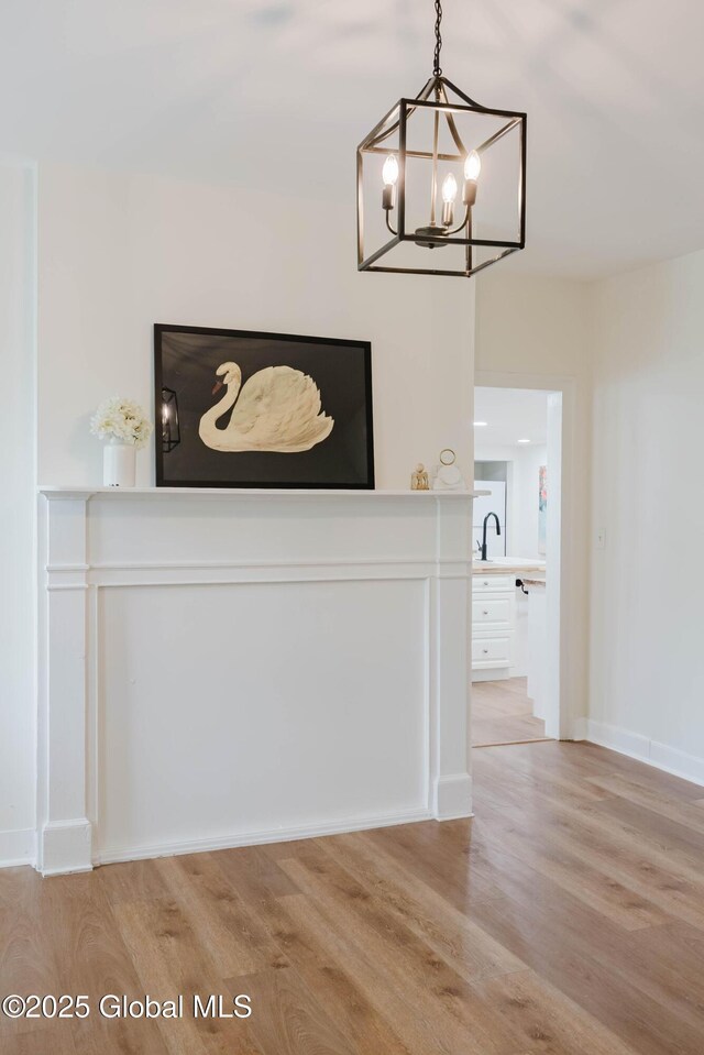 unfurnished dining area featuring light wood-type flooring, a chandelier, a sink, and baseboards