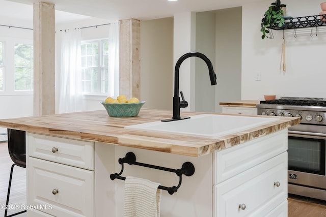detailed view of wood counters, high end stainless steel range, a sink, and white cabinets