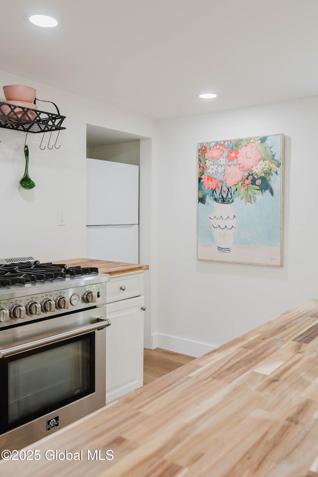 kitchen featuring high end stove, light wood-type flooring, white cabinets, baseboards, and wooden counters