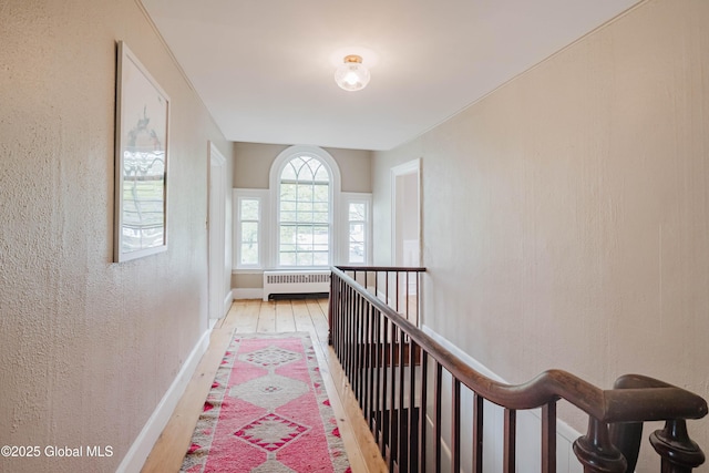 corridor with radiator heating unit, light wood finished floors, an upstairs landing, a textured wall, and baseboards