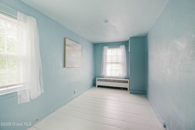 empty room featuring radiator heating unit, wood finished floors, and baseboards