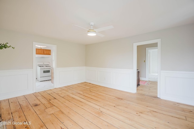 empty room featuring a ceiling fan, light wood-style flooring, and a wainscoted wall