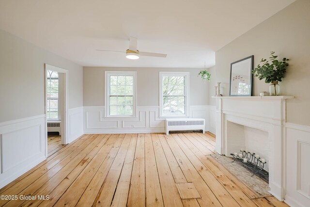 living area featuring radiator heating unit, a wainscoted wall, ceiling fan, wood-type flooring, and a decorative wall