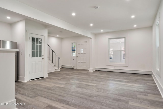 unfurnished living room with baseboard heating, recessed lighting, wood finished floors, a baseboard heating unit, and stairway