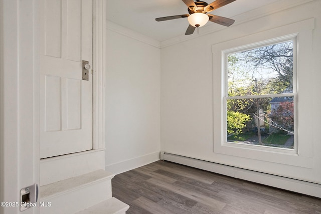 empty room with crown molding, a ceiling fan, a baseboard heating unit, and dark wood-style flooring