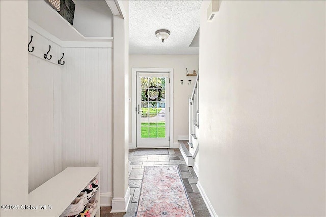mudroom featuring baseboards, stone tile floors, and a textured ceiling