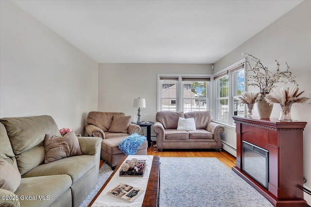 living area featuring light wood-style flooring, a baseboard radiator, and a glass covered fireplace