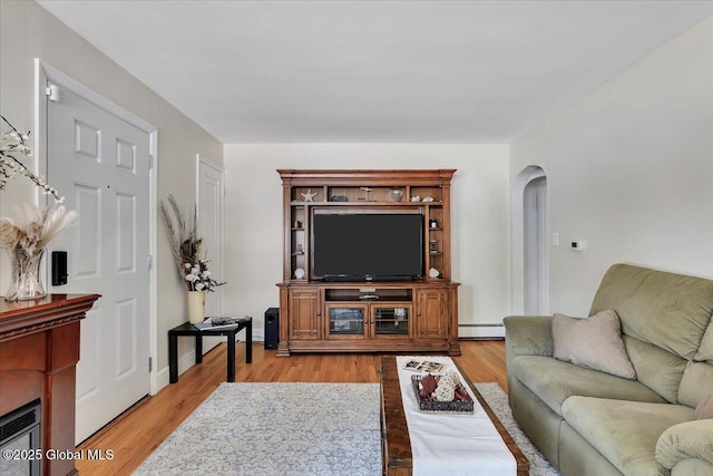 living room featuring a baseboard heating unit, arched walkways, and light wood-style floors