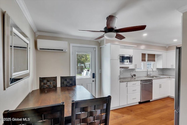 kitchen featuring appliances with stainless steel finishes, a wall mounted AC, a ceiling fan, white cabinetry, and crown molding