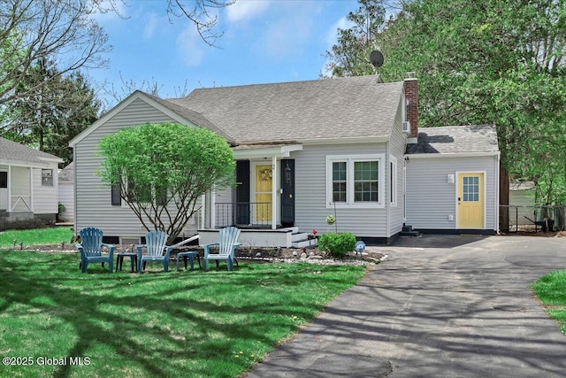 view of front of home with a chimney, a front yard, driveway, and roof with shingles