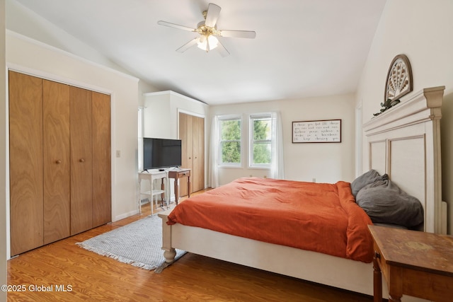 bedroom with two closets, vaulted ceiling, and wood finished floors