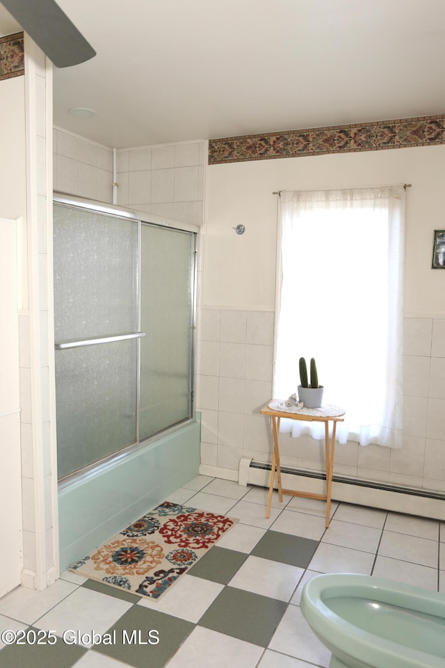 bathroom with bath / shower combo with glass door, a bidet, baseboard heating, and tile walls