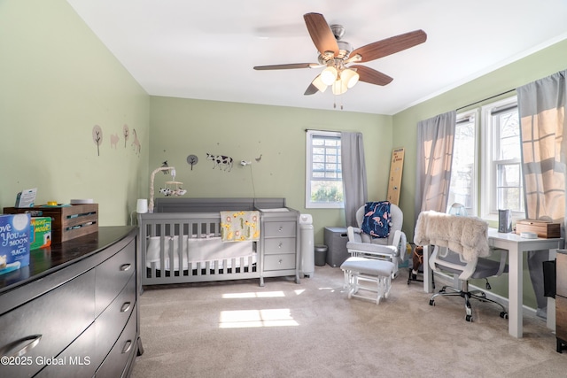 bedroom with a ceiling fan, light colored carpet, and a crib