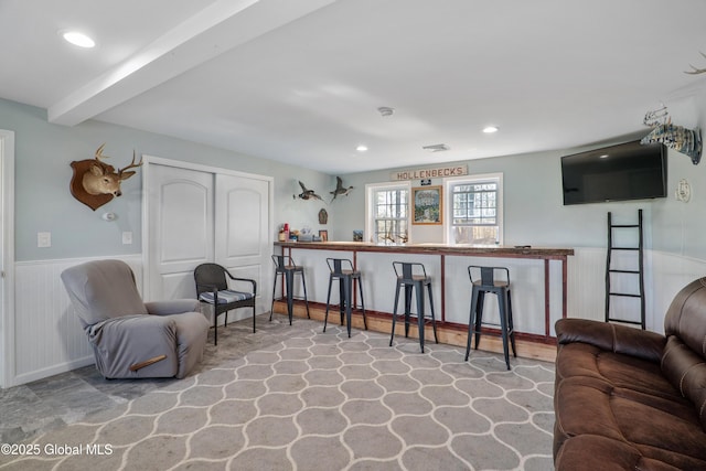 interior space with a wainscoted wall, bar area, recessed lighting, and beam ceiling