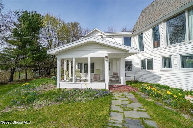exterior space with covered porch, a shingled roof, and a front lawn