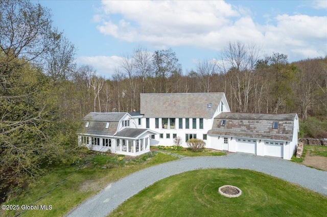 view of front of home with a view of trees, driveway, a gambrel roof, and a front lawn