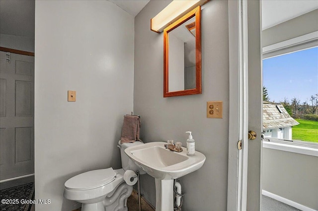 half bath featuring baseboards and toilet
