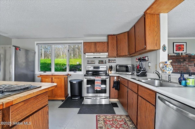 kitchen with light countertops, a textured ceiling, under cabinet range hood, a sink, and appliances with stainless steel finishes