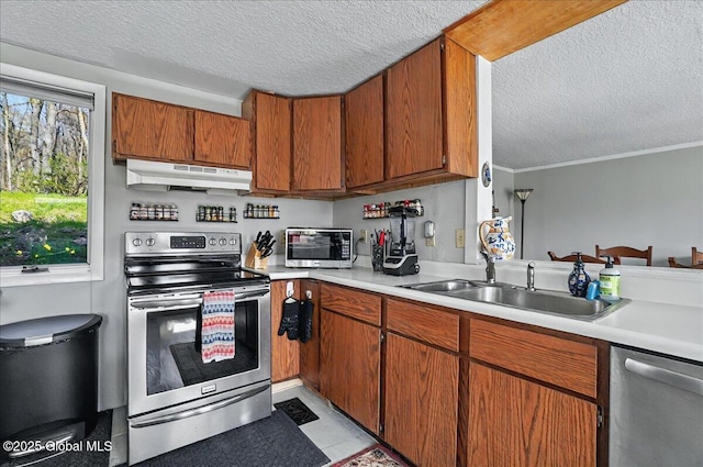 kitchen featuring under cabinet range hood, a textured ceiling, appliances with stainless steel finishes, and a sink