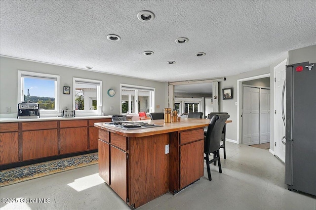 kitchen featuring a textured ceiling, appliances with stainless steel finishes, a center island, brown cabinets, and light countertops