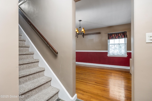 stairs with baseboards, wood finished floors, and a notable chandelier