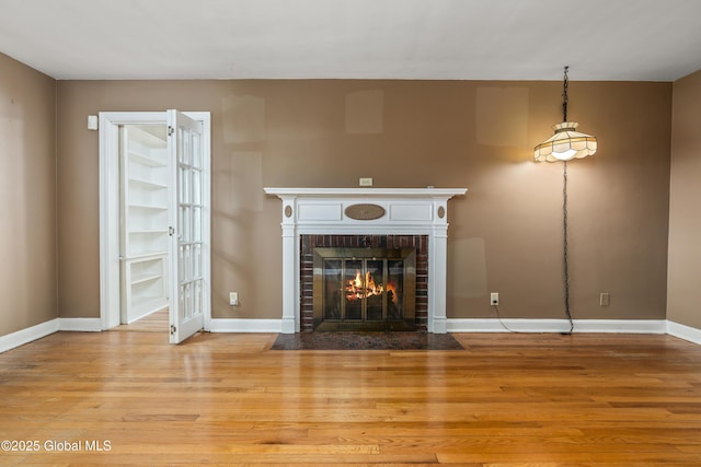 unfurnished living room with a brick fireplace, baseboards, and wood finished floors