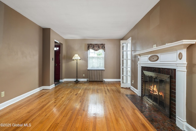unfurnished living room featuring a brick fireplace, baseboards, radiator heating unit, and hardwood / wood-style floors