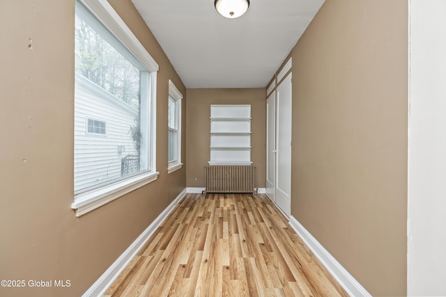 hallway with baseboards, light wood-style flooring, and radiator heating unit