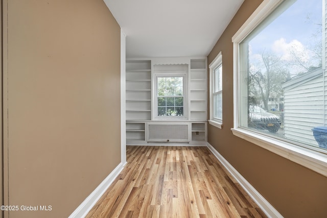 unfurnished room featuring baseboards, light wood finished floors, radiator heating unit, and built in features