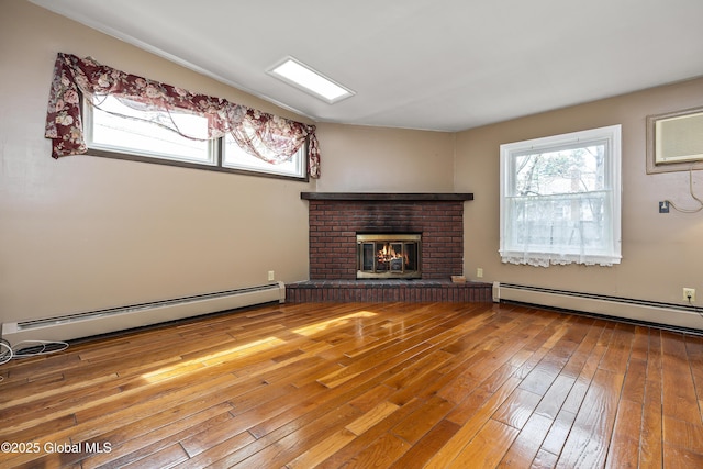 unfurnished living room featuring a healthy amount of sunlight, baseboard heating, a brick fireplace, and hardwood / wood-style floors