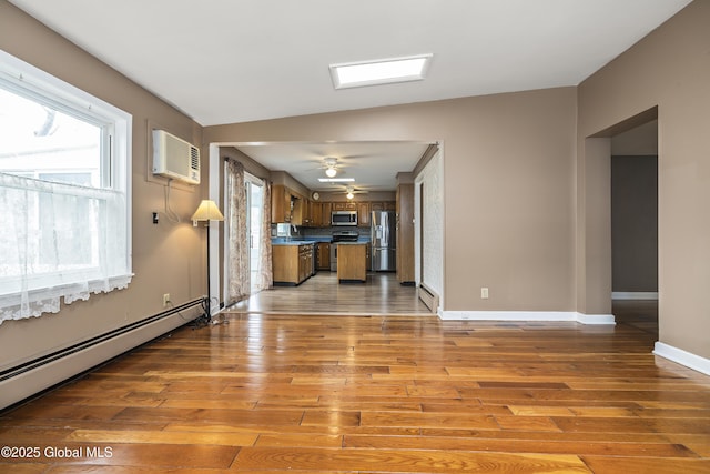 unfurnished living room with wood-type flooring, baseboards, a wall unit AC, and baseboard heating