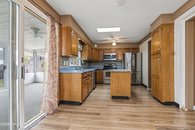 kitchen with brown cabinets, a sink, light wood finished floors, stainless steel appliances, and a ceiling fan