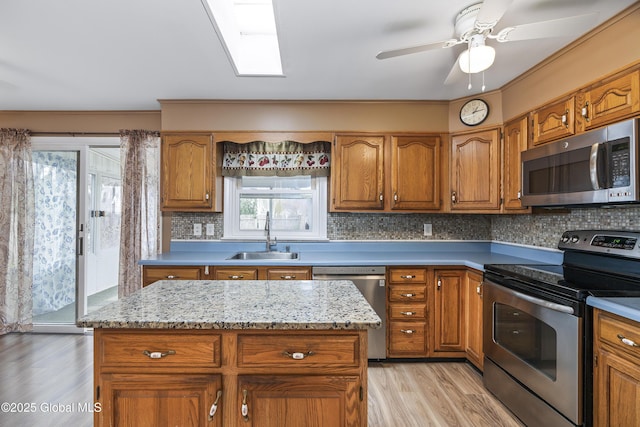 kitchen with brown cabinets, a sink, light wood finished floors, appliances with stainless steel finishes, and backsplash
