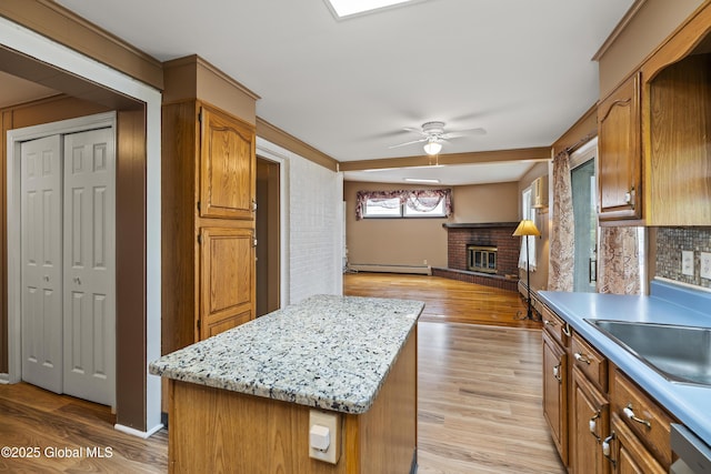 kitchen with light wood-style floors, a baseboard radiator, a brick fireplace, and ceiling fan