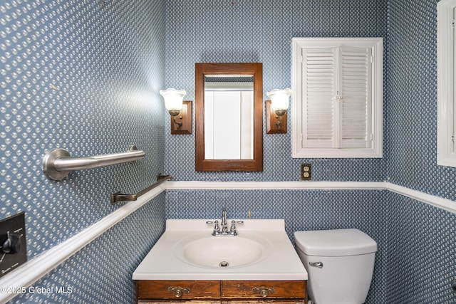 half bath with vanity, toilet, and wallpapered walls