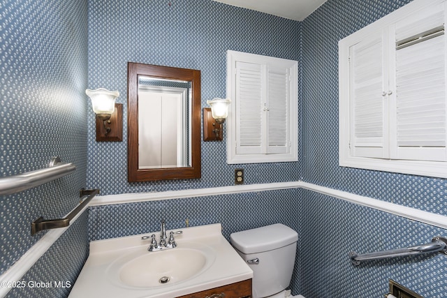 half bath featuring vanity, toilet, and wallpapered walls