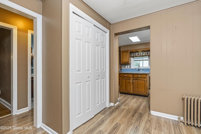 hall with radiator heating unit, baseboards, light wood-type flooring, and a sink