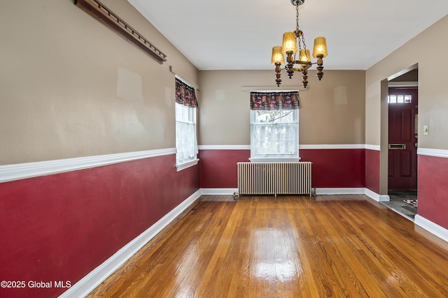 unfurnished room with an inviting chandelier, baseboards, radiator heating unit, and hardwood / wood-style flooring