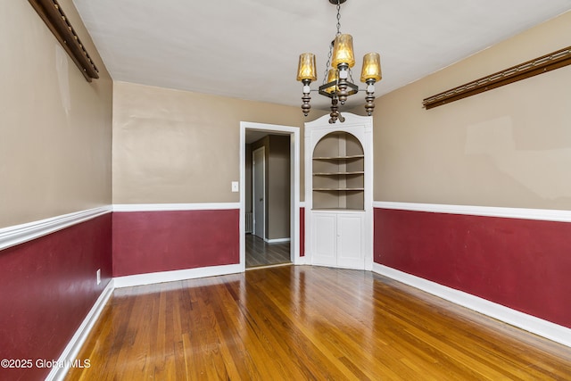 unfurnished dining area with baseboards, an inviting chandelier, built in shelves, and wood finished floors